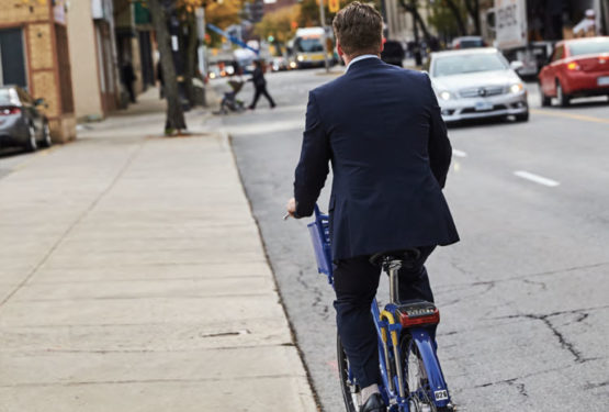 A man in a business suit riding a bicycle down a busy street