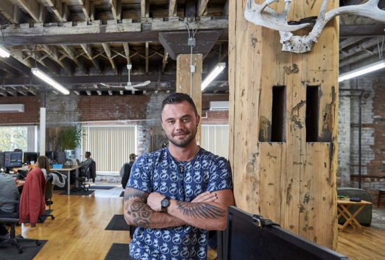 A portrait of a man standing in a creative office space in a reclaimed industrial building.