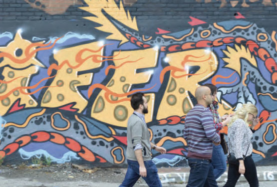 A group of people walking past a wall with colourful graffiti.