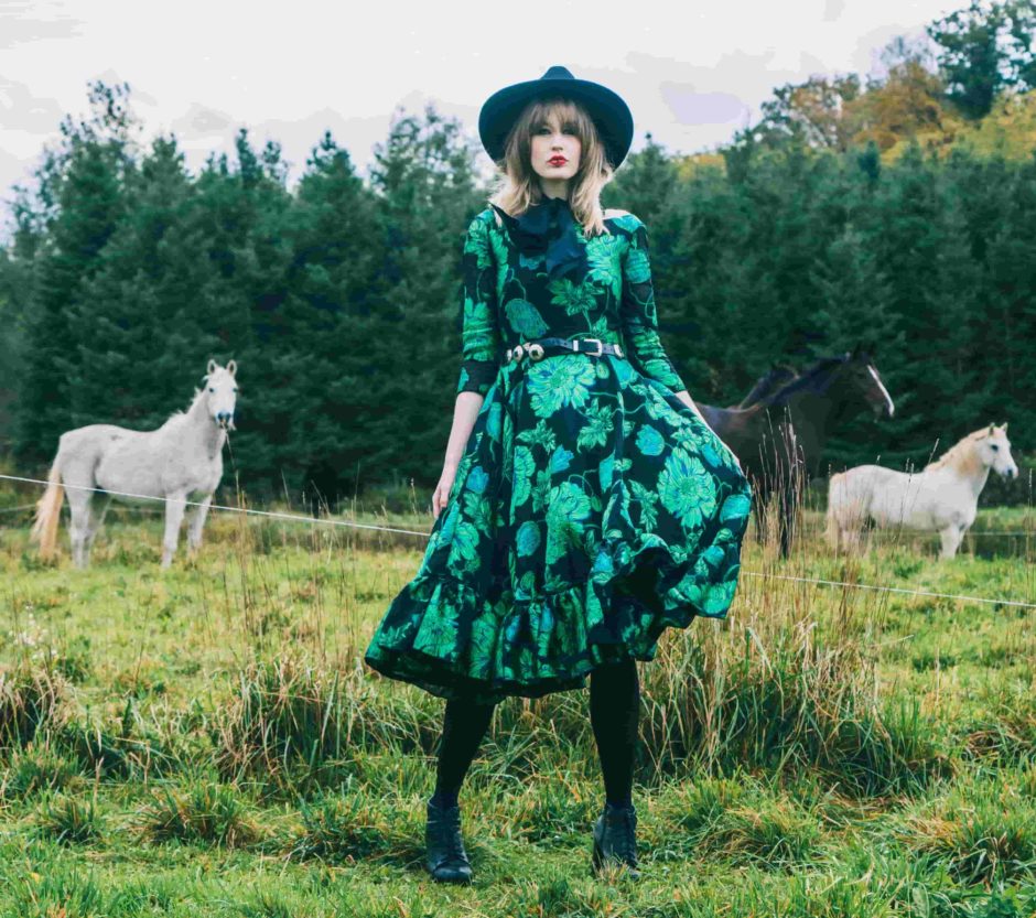 woman in a green and black dress in a field with horses