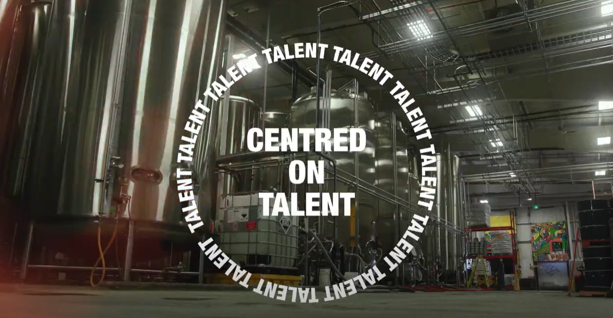 Industrial interior with large metal tanks. Text overlay reads "CENTRED ON TALENT" surrounded by repeated word "TALENT.