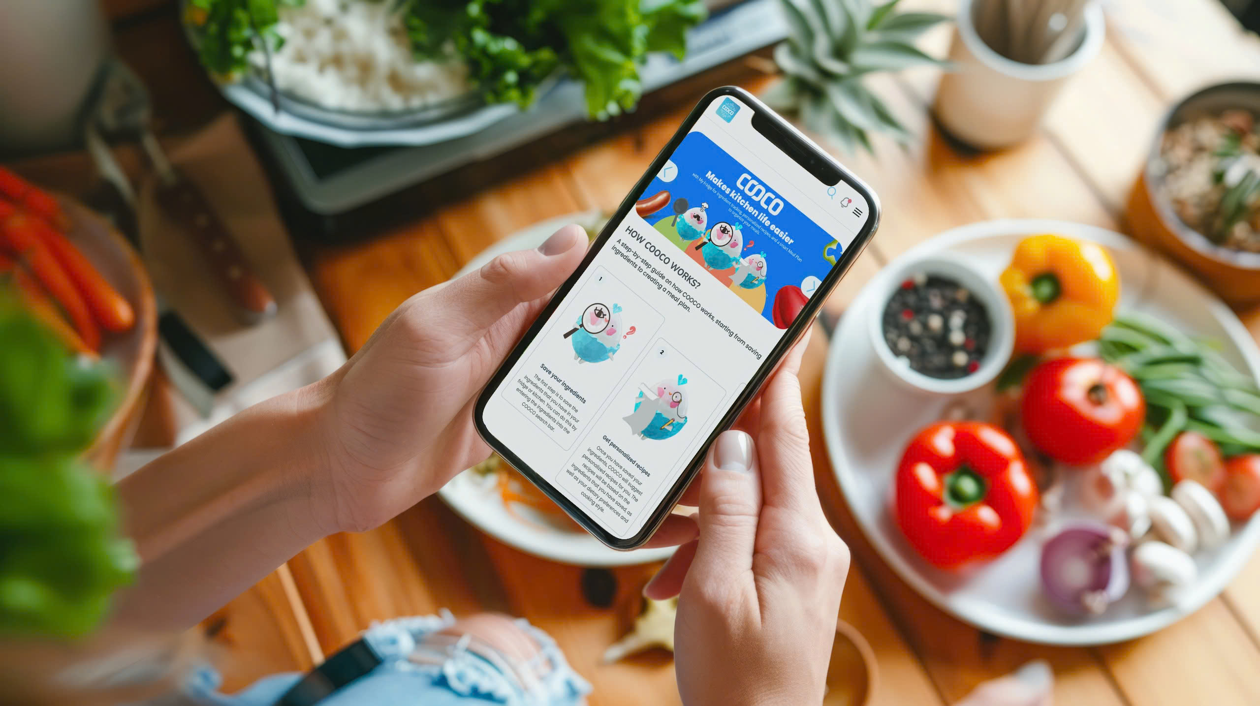 Person holding a smartphone displaying a colorful app while sitting at a table with fresh vegetables and kitchen items.