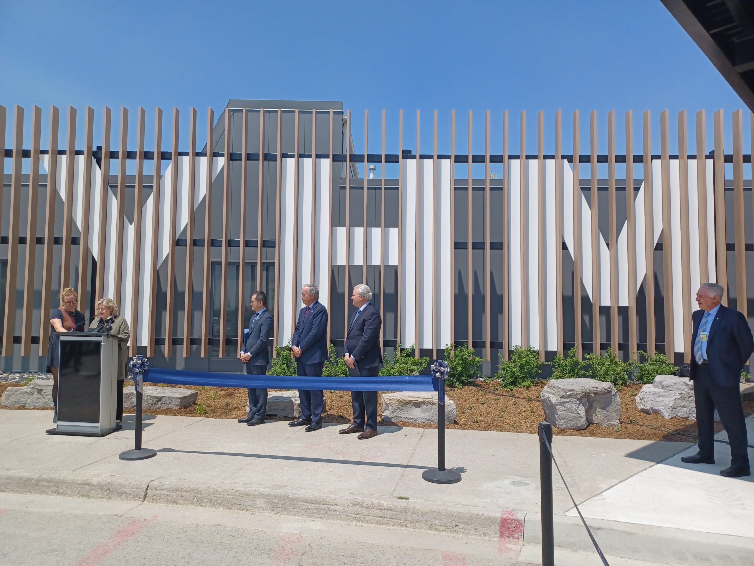 Several people stand in front of a modern building facade with large "Y, F, M" letters during a ribbon-cutting event.