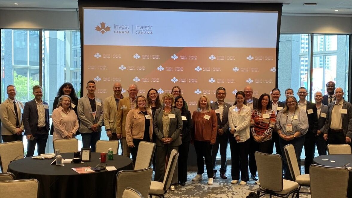 A group of people pose for a photo in front of a Canada-themed backdrop at an indoor business event.