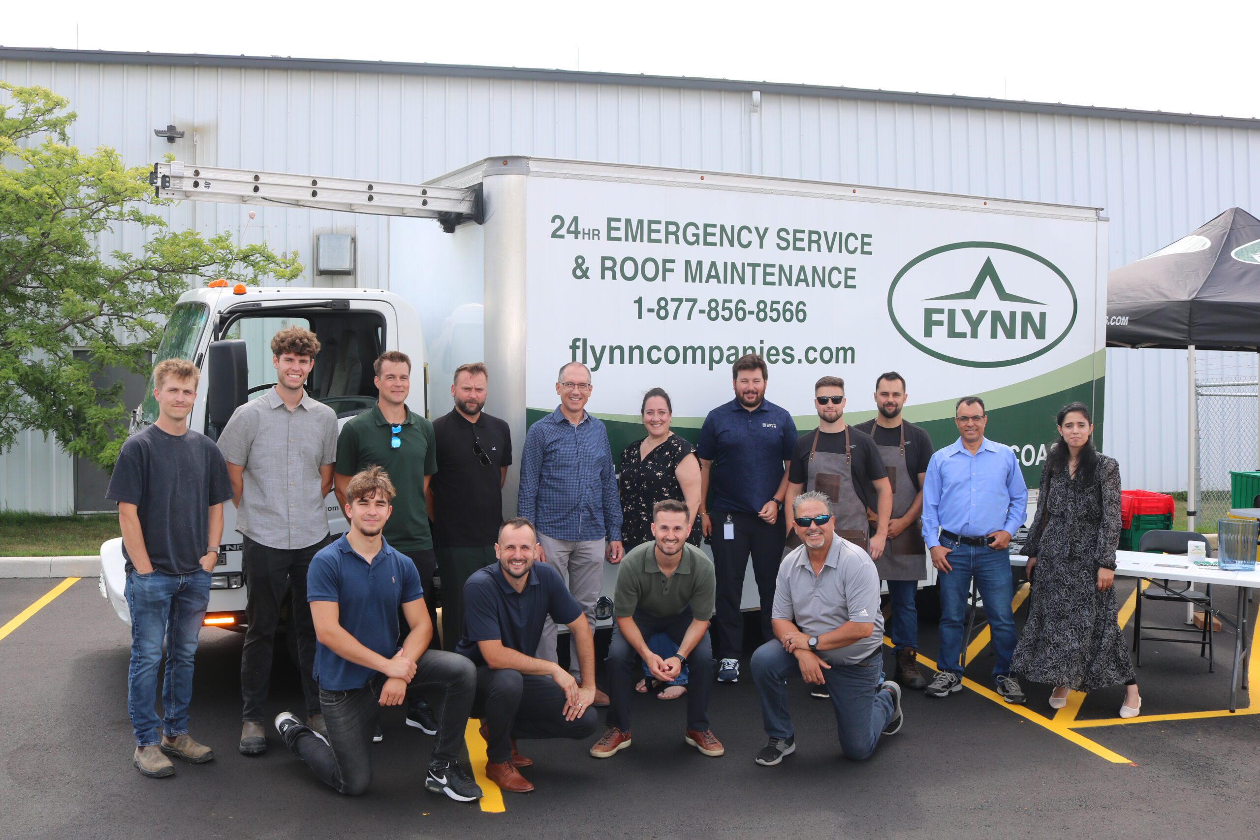 A group of people pose in front of a Flynn Companies service truck in a parking lot, some smiling at the camera.