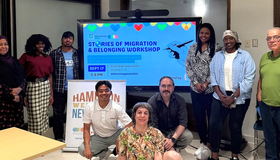 A group of people standing in front of a screen with the words: "Stories of Migration & Belonging Workshop"