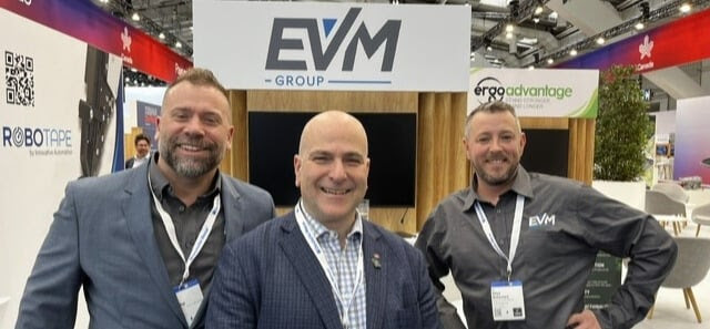Three men standing in front of the EVM Group booth at a trade show