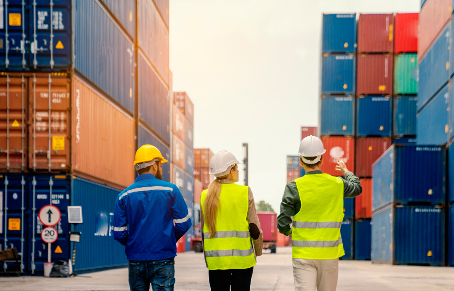 Three people standing between stacked cargo containers.